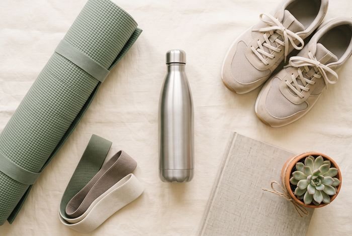A flat lay of a water bottle, yoga mat, resistance band, walking shoes and a notebook